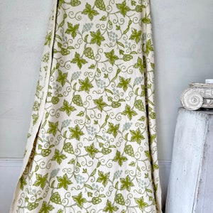 May include: White fabric with a green vine and leaf pattern. The fabric has a subtle texture and a slightly distressed look.
