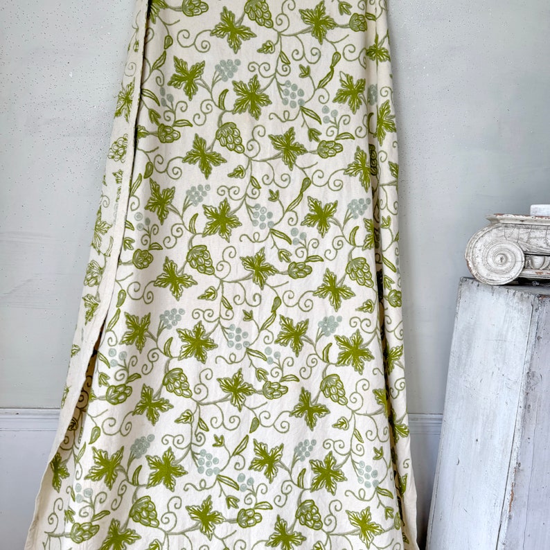 May include: White fabric with a green vine and leaf pattern. The fabric has a subtle texture and a slightly distressed look.