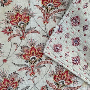 May include: A white cotton quilt with a floral pattern in shades of red and black. The quilt is made with a patchwork design and has a quilted texture.
