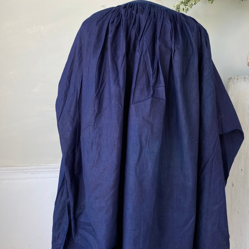 May include: A navy blue cotton tunic with a gathered neckline and a loose, flowing silhouette.
