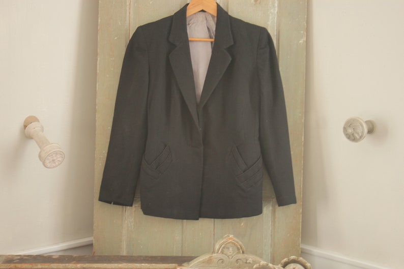 May include: A black blazer with a single button closure and decorative stitching on the pockets.