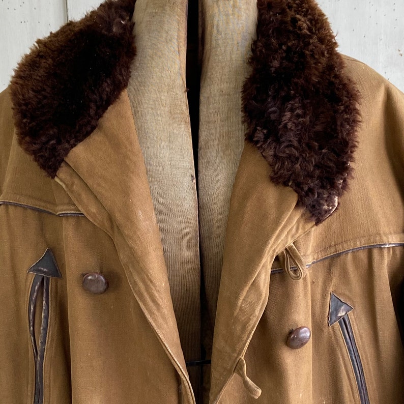 May include: A brown, vintage-style jacket with a fur collar. The jacket has a double-breasted closure with two buttons and a leather trim around the edges.