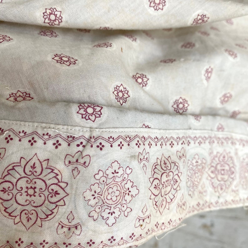 K&ouml;nnte beinhalten: Nahaufnahme eines wei&szlig;en Stoffes mit rotem Blumenmuster. Der Stoff hat einen Rand mit einem komplizierteren Muster.