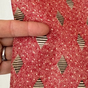 May include: Red fabric with a white and black diamond pattern. The fabric has a textured surface.