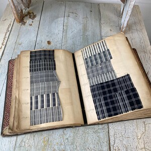 May include: A vintage fabric sample book with black and white striped and plaid fabric swatches. The book is open to two pages, each with a numbered list of fabric samples.