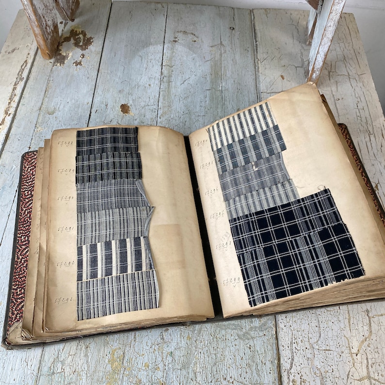 May include: A vintage fabric sample book with black and white striped and plaid fabric swatches. The book is open to two pages, each with a numbered list of fabric samples.