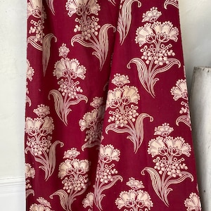 Könnte beinhalten: Burgunderfarbener Stoff mit einem cremefarbenen Blumenmuster. Das Design zeigt stilisierte Blumen und Blätter, die einen klassischen Look erzeugen. Der Stoff eignet sich für Polster oder Vorhänge. Das Muster wiederholt sich.