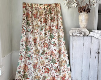 May include: A white fabric curtain with a large-scale floral print in shades of red, orange, green, and brown. The curtain is hanging from a rod and is draped on the floor.
