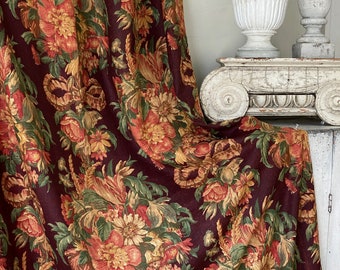 Può includere: Un tessuto color borgogna con un motivo floreale in tonalità di rosso, arancio e giallo. Il tessuto ha un aspetto testurizzato, simile al lino.