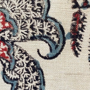 Pu&ograve; includere: Primo piano di un tessuto con un motivo paisley in tonalit&agrave; di nero, blu e rosso su uno sfondo beige.