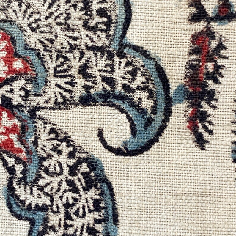 Pu&ograve; includere: Primo piano di un tessuto con un motivo paisley in tonalit&agrave; di nero, blu e rosso su uno sfondo beige.