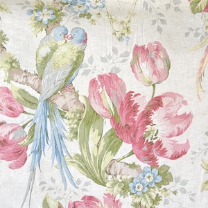May include: A white fabric with a floral pattern featuring pink tulips, blue forget-me-nots, and green leaves. Two blue and green parrots are perched on a branch.