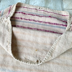 May include: A vintage, off-white linen sack with a striped pattern in shades of pink and gray. The sack is folded in half, revealing the inside of the fabric.