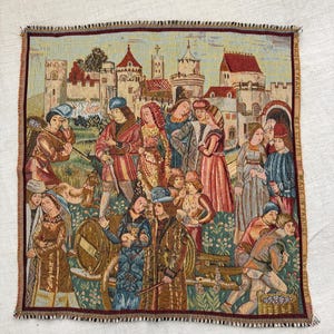 May include: A tapestry depicting a medieval scene with figures in period clothing, set against a backdrop of castles and buildings. The artwork features a variety of colors, including reds, blues, and greens, with a textured appearance. The tapestry is square with a fringed edge.