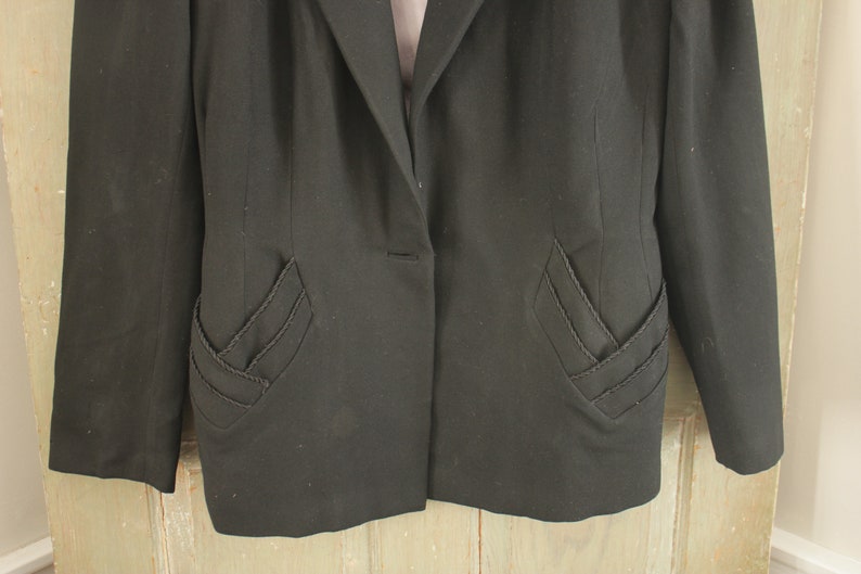 May include: A black blazer with a single button closure and unique, decorative stitching on the pockets.