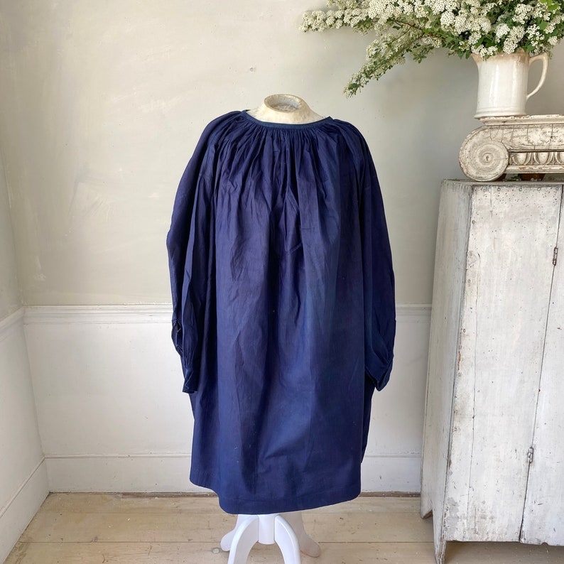 May include: A navy blue smock dress with a gathered neckline and long sleeves. The dress is made of a soft, lightweight fabric and has a relaxed fit.
