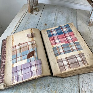 May include: An open book with fabric swatches in various plaid patterns. The swatches are in shades of blue, red, brown, and purple. The book is open to a page with handwritten notes and numbers.