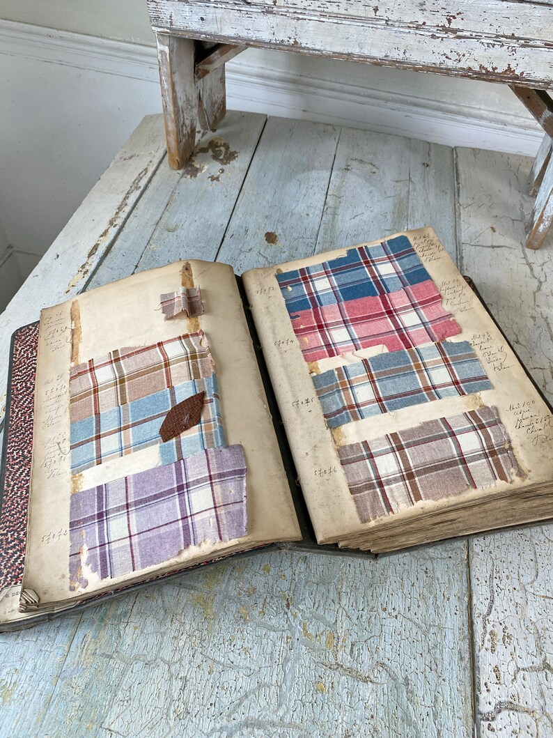 May include: An open book with fabric swatches in various plaid patterns. The swatches are in shades of blue, red, brown, and purple. The book is open to a page with handwritten notes and numbers.