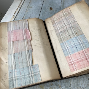 May include: A vintage fabric swatch book with numbered pages and various fabric samples. The samples include a red and white plaid, a blue and white plaid, and a light blue and white plaid.