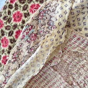 May include: Close-up of several antique fabric swatches. One features pink roses on a cream background, another has a floral pattern with burgundy and blue accents, and others have small repeating patterns in pink and cream.