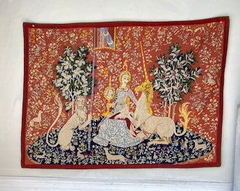 May include: A tapestry depicting a scene from the Lady and the Unicorn series. A woman in a blue dress sits on a throne with a unicorn and a lion beside her. The tapestry is woven with intricate details and vibrant colors.