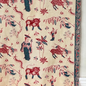 Könnte beinhalten: Cremefarbener Stoff mit einem sich wiederholenden Muster aus rot- und türkis-asiatisch inspirierten Figuren, Tigern, Insekten und Blättern. Der Stoff hat einen türkisfarbenen Rand mit einem floralen Design. Das Gesamtdesign erinnert an ein Vintage-Textil.