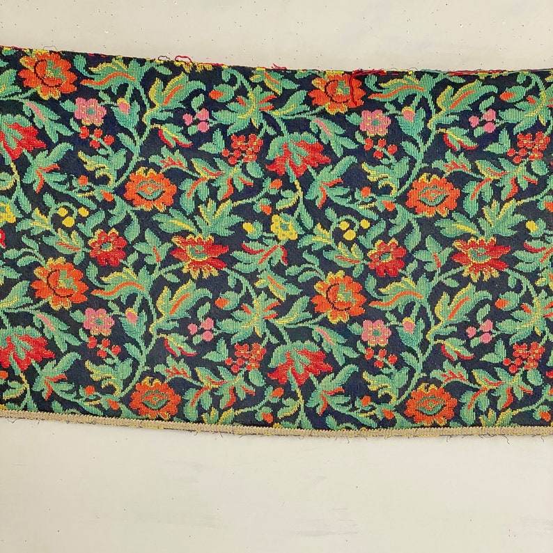 May include: A close-up of a fabric with a floral pattern. The fabric is dark blue with green, red, orange, and yellow flowers. The fabric has a textured surface.