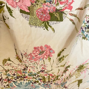 May include: A white fabric with a floral pattern featuring pink, green, and blue flowers. The fabric has a vintage aesthetic.
