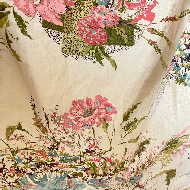 May include: A white fabric with a floral pattern featuring pink, green, and blue flowers. The fabric has a vintage aesthetic.