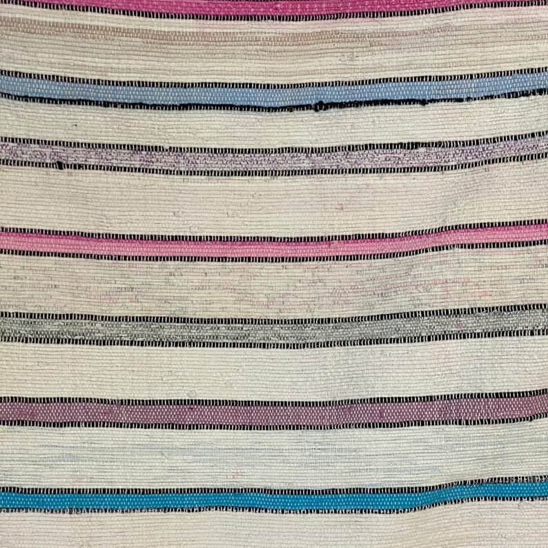 May include: A close-up of a woven fabric with horizontal stripes in shades of pink, blue, gray, and white.