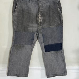 May include: Gray corduroy pants with multiple patches of different fabrics. The pants have a button fly and two front pockets.