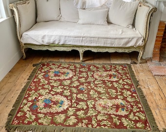 Può includere: Un tappeto vintage con motivo floreale e frange verdi, steso su un pavimento in legno davanti a un divano letto bianco con biancheria da letto in lino bianco.