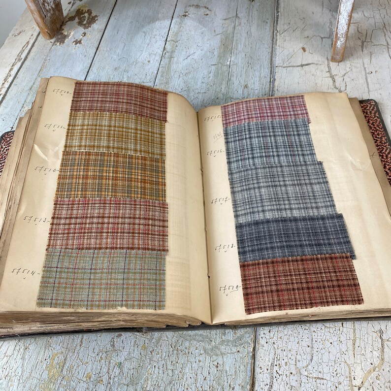 May include: An open book with fabric swatches. The swatches are in various shades of brown, blue, and gray. The book has handwritten numbers on the pages.