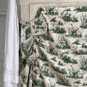 Op de afbeelding: Een witte stoffen kap met een groen-wit toile-patroon met een herhalend ontwerp van mensen en bomen. De kap is bovenaan geplooid en heeft een decoratieve ronde afwerking.