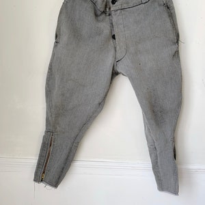 May include: A pair of gray riding breeches with a zipper on the lower leg and a button fly.