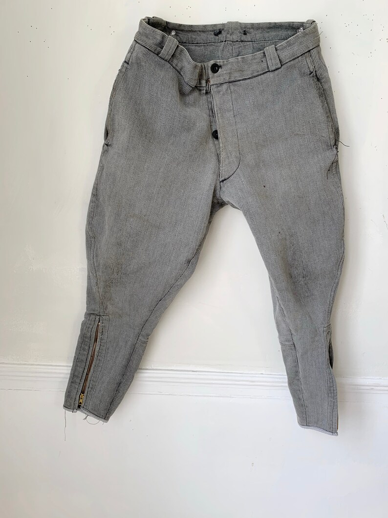 May include: A pair of gray riding breeches with a zipper on the lower leg and a button fly.