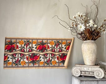 May include: A vintage floral wallpaper roll featuring a repeating pattern of red apples and yellow flowers within a gray lattice design. The wallpaper is partially unrolled, revealing its aged paper backing. A vase of flowers sits on a decorative stand.