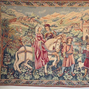 May include: A tapestry depicting a medieval scene with figures on horseback and in period clothing. The artwork features a castle, trees, and a river, with a border of floral and geometric patterns. The color palette includes reds, greens, and blues.