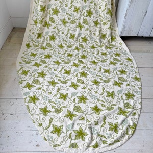 May include: A white tablecloth with a green vine and grape pattern. The tablecloth is oval shaped and has a scalloped edge.