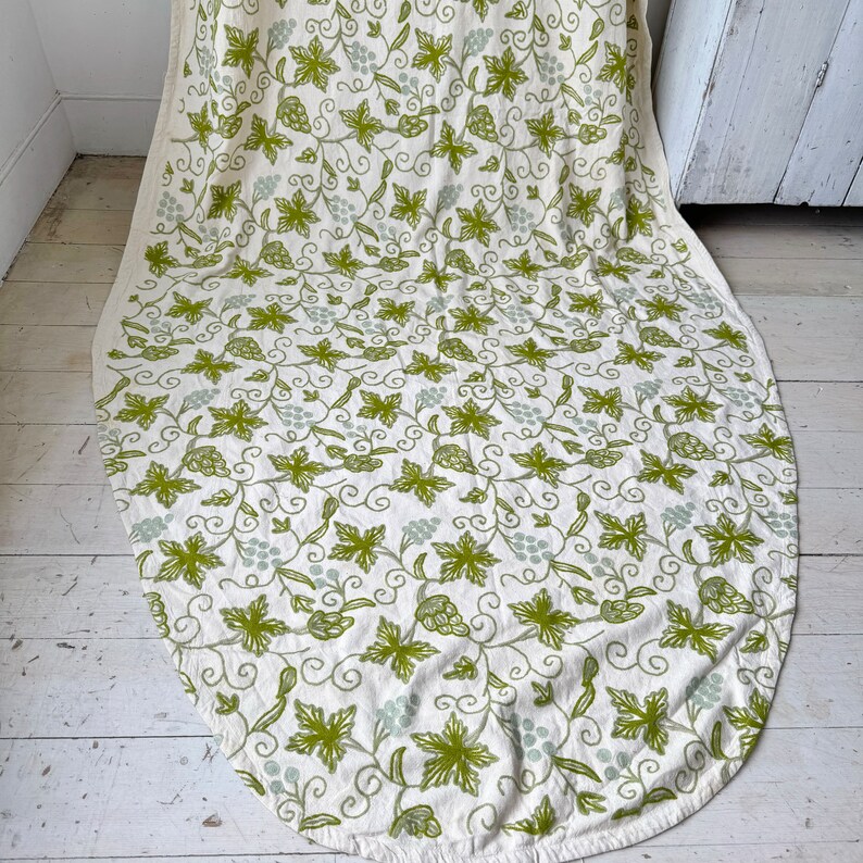 May include: A white tablecloth with a green vine and grape pattern. The tablecloth is oval shaped and has a scalloped edge.