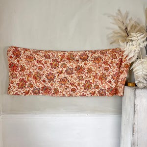 Può includere: Un tessuto bianco con un motivo floreale rosso, arancione e blu. Il tessuto è appeso a un muro.