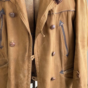 May include: A brown canvas jacket with a fur-lined collar and multiple pockets. The jacket has a double-breasted closure with brown buttons and a drawstring at the waist.