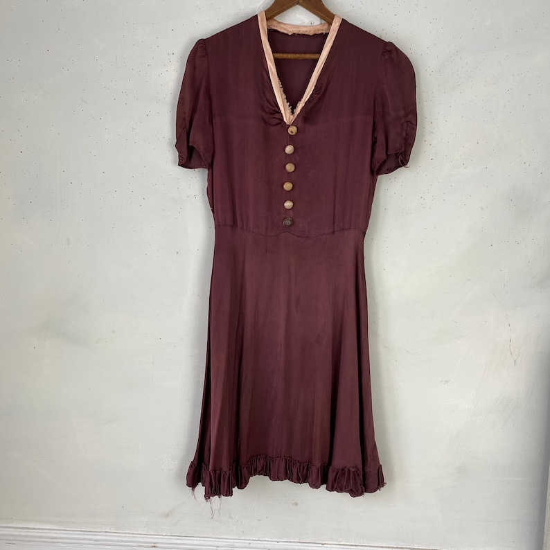 May include: A maroon vintage dress with a pink lace trim around the neckline and short sleeves. The dress has a button-up front and a ruffled hem.