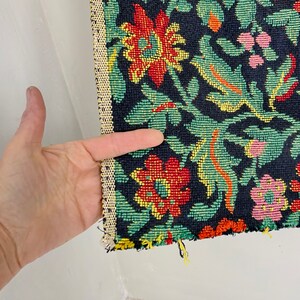 May include: Close-up of a black fabric with a floral pattern. The flowers are red, yellow, green, and pink. The fabric has a textured surface.