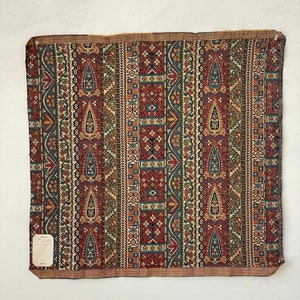 Könnte beinhalten: Ein Vintage-Stoffmuster mit einem sich wiederholenden Muster aus Paisley-Motiven, geometrischen Formen und floralen Designs in Rot-, Blau-, Grün- und Cremetönen. Der Stoff hat eine gewebte Textur und ein leicht verblichenes Aussehen.