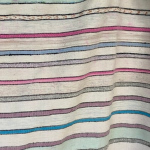 May include: A white woven fabric with horizontal stripes in shades of pink, blue, and gray. The fabric is folded and has a textured surface.