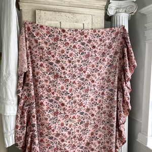 May include: A pink fabric with a small floral print in shades of red, brown, and black. The fabric has a ruffled edge.