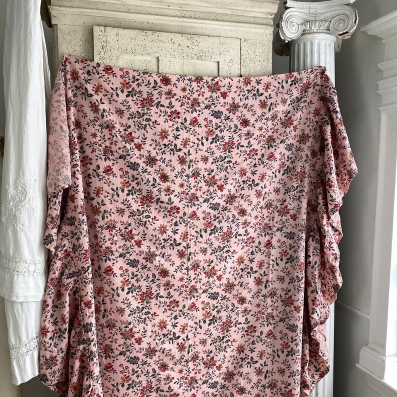 May include: A pink fabric with a small floral print in shades of red, brown, and black. The fabric has a ruffled edge.