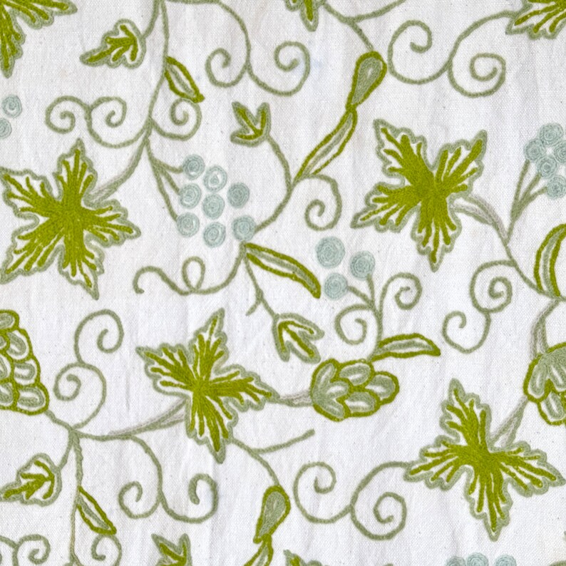 May include: White fabric with an embroidered design of green leaves and vines. The design is reminiscent of a grapevine.