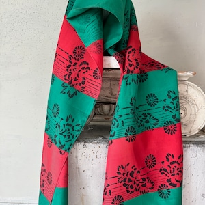 Peut inclure: Une écharpe rayée verte et rouge avec un motif floral. L'écharpe est en tissu doux et soyeux et a une bordure frangée.
